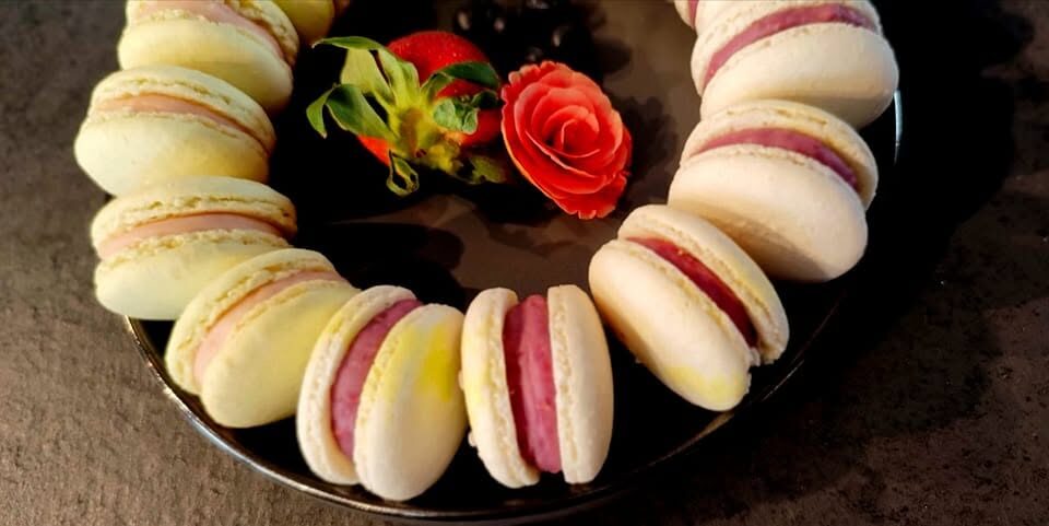 Coroană de macarons pe platou negru, cu un trandafir de zahăr la mijloc